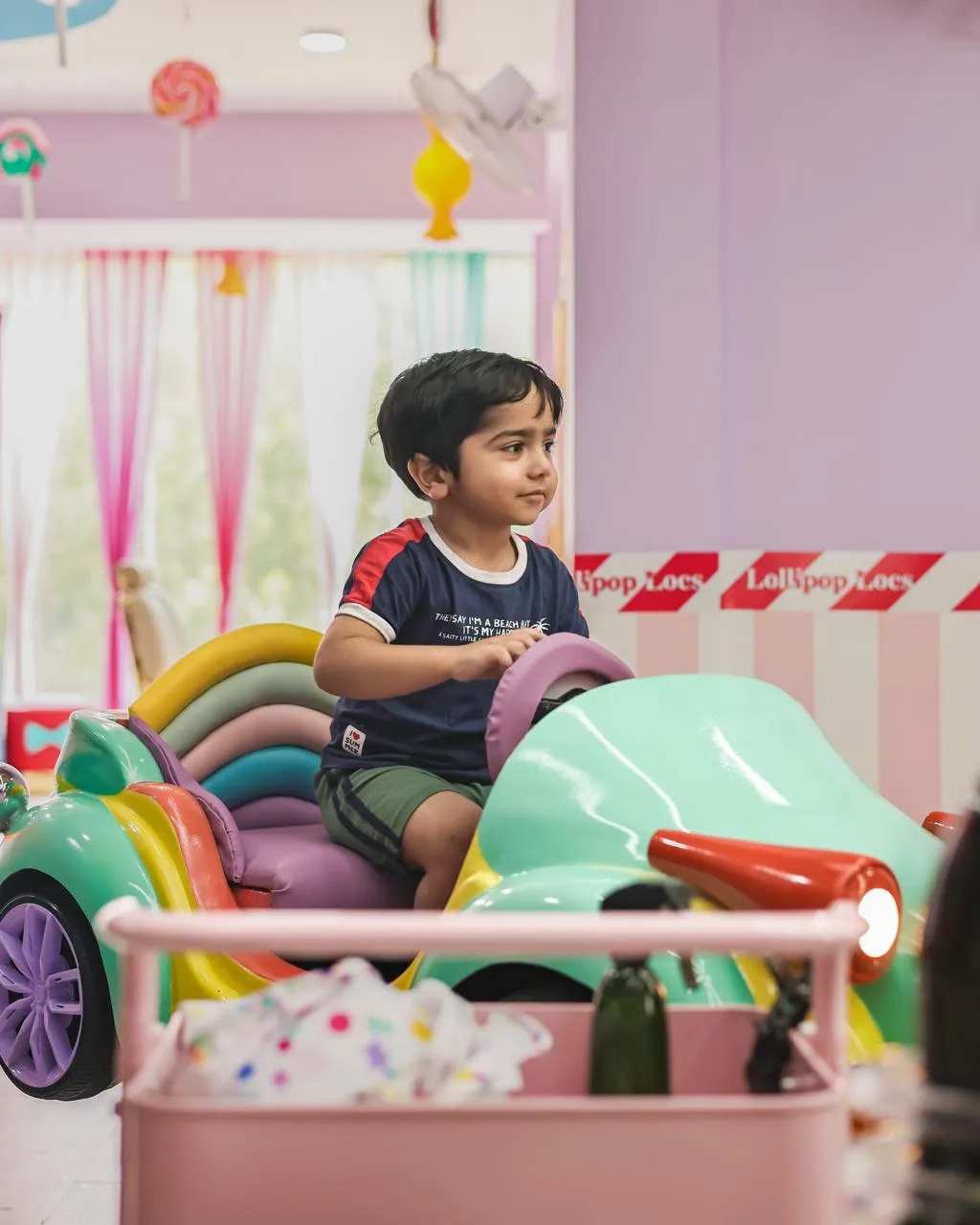 Child seated in the rainbow car haircut chair at Lollipop Locs