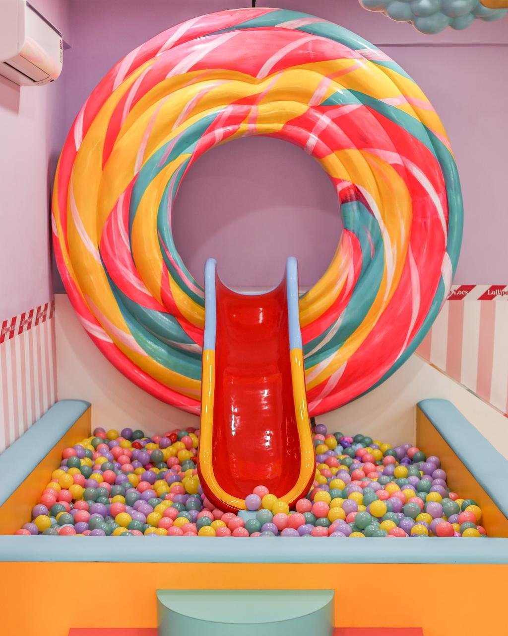 Giant swirled lollipop slide leading into a colourful ball pit at Lollipop Locs